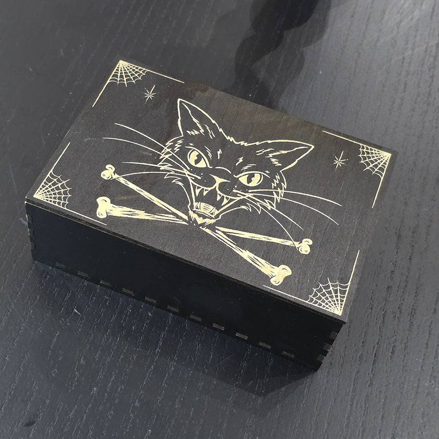 Black box with cat and bones engraved on a dark surface