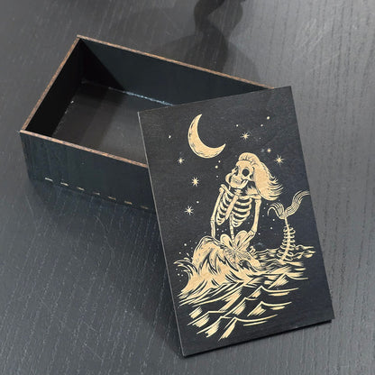 Black wooden box with a skeleton mermaid design engraved on a dark surface